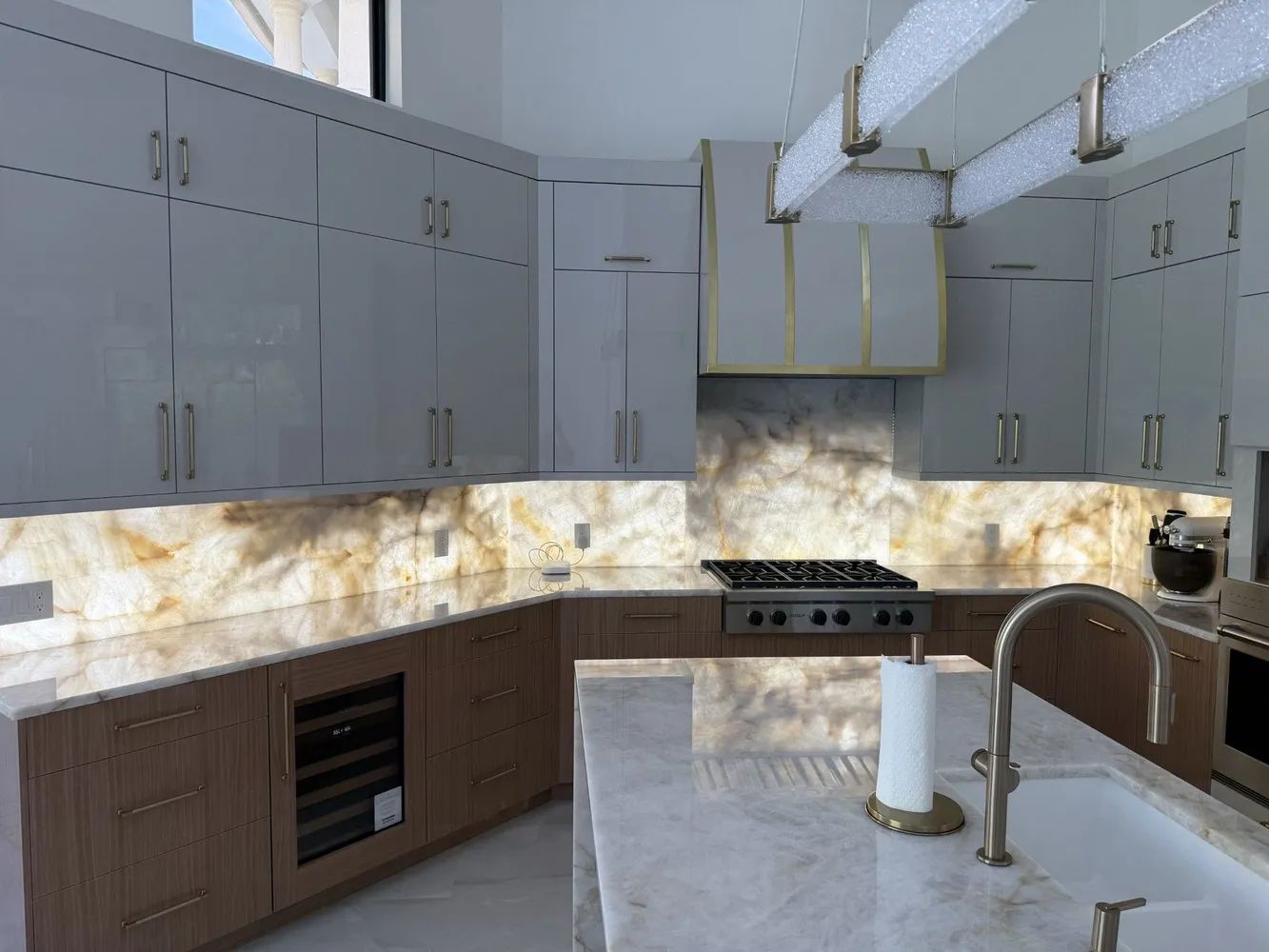 Modern kitchen with white cabinets, dark wood lower cabinets, stone backsplash, and a large island sink