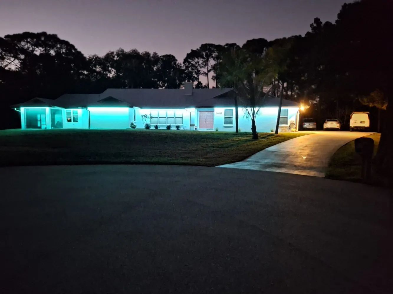 Single-story house at night with bright blue porch lights and a curved driveway leading to the garage.