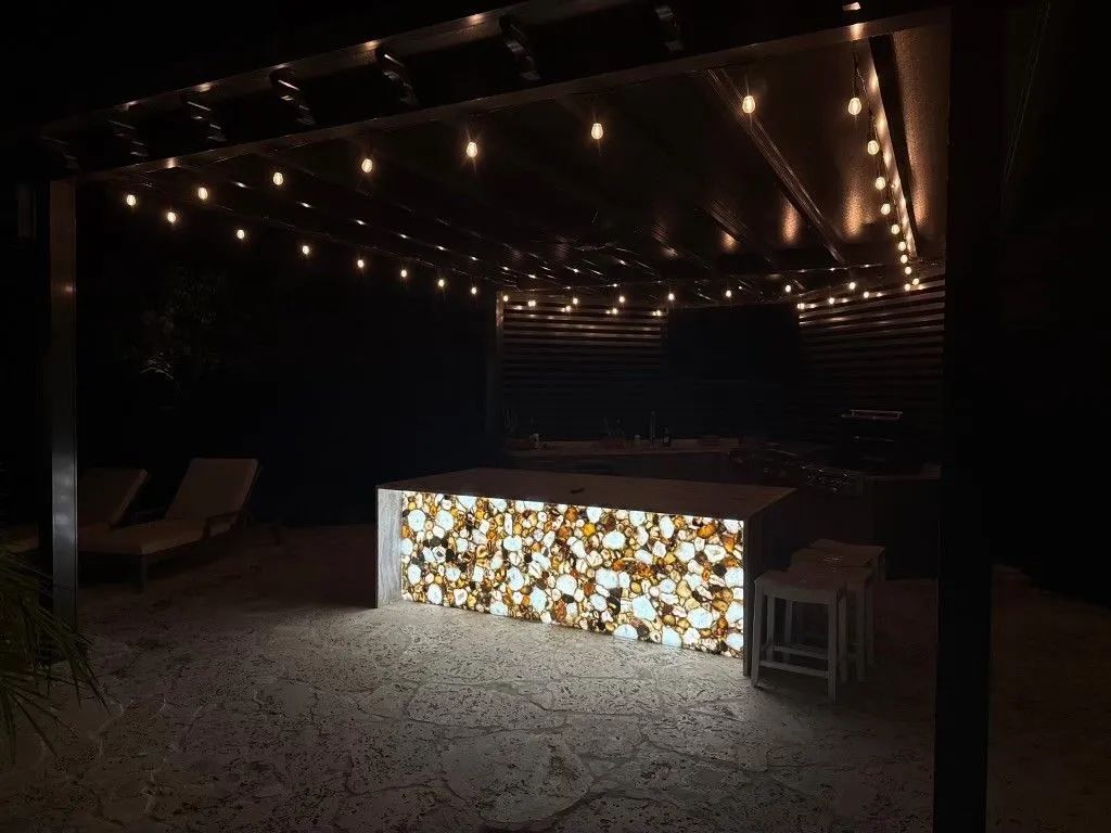 Outdoor patio bar with string lights and a glowing floral-front counter at night