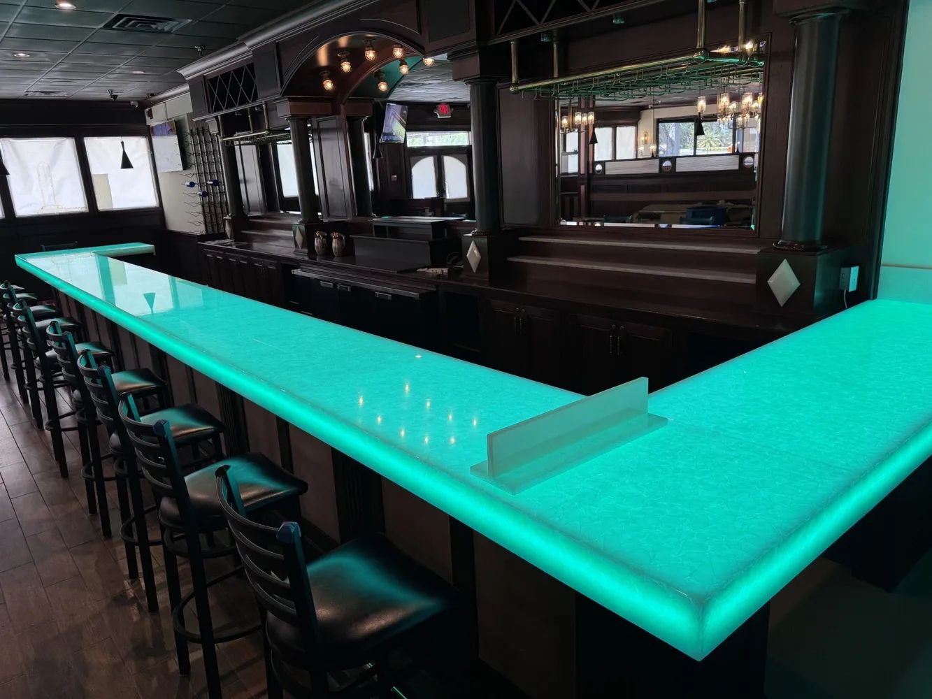 Empty bar with glowing turquoise countertop and stools in a dimly lit lounge