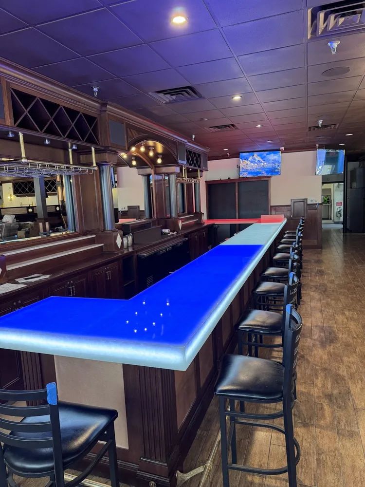 Empty bar interior with glowing blue countertop and stools under warm ceiling lights.