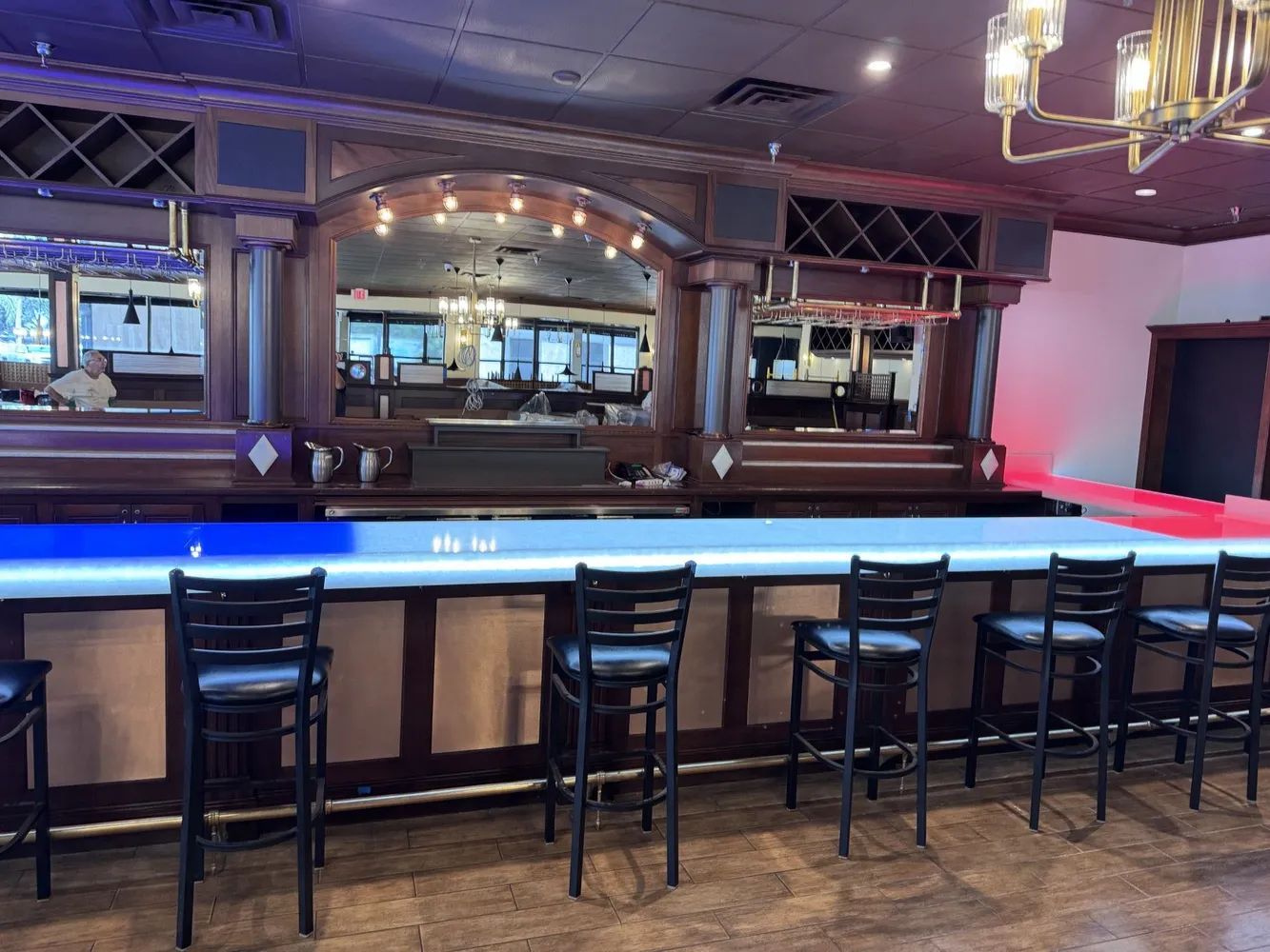 Empty bar with blue-lit counter, stools, mirrors, and purple ambient lighting.