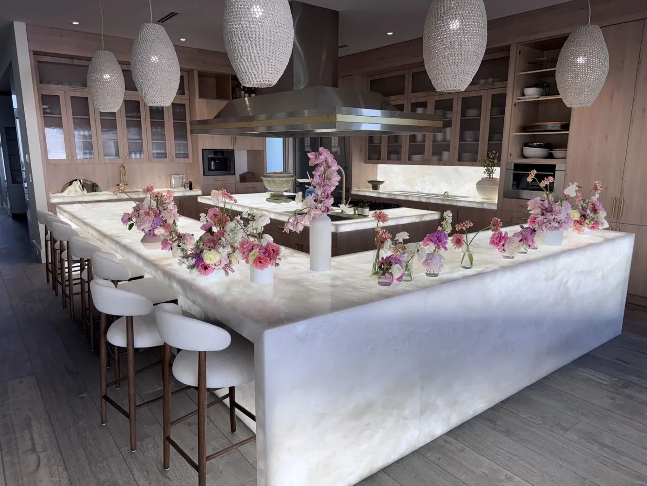 Elegant banquet hall with a marble bar, pink floral centerpieces, and hanging white pendant lights