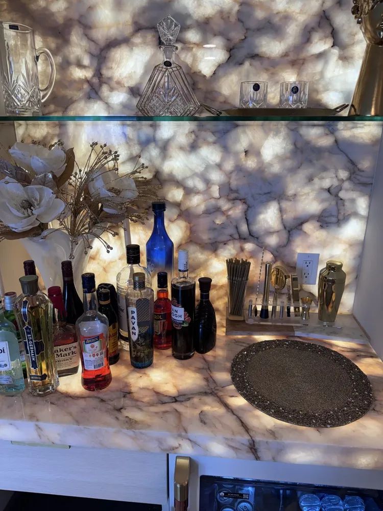 Bar with assorted liquor bottles on a marble counter, backlit by decorative wall lighting.
