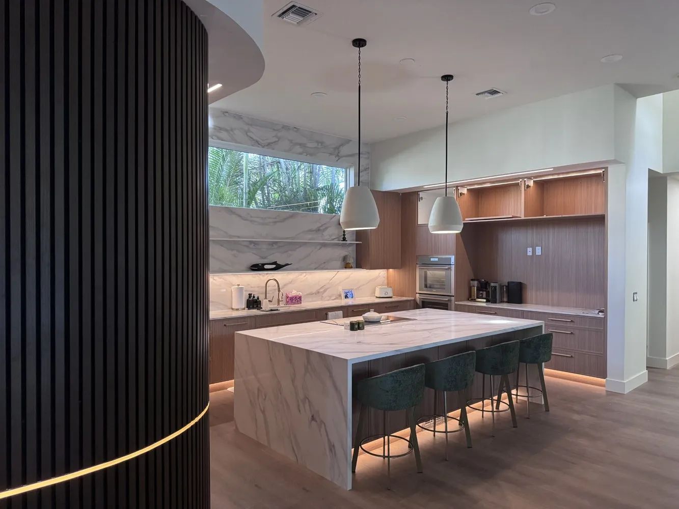 Modern kitchen with marble island, pendant lights, wood cabinets, and a black slatted column