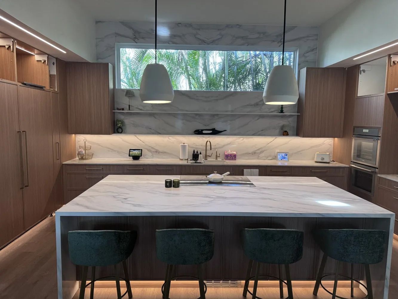 Modern kitchen with large marble island, wood cabinets, pendant lights, and four teal stools