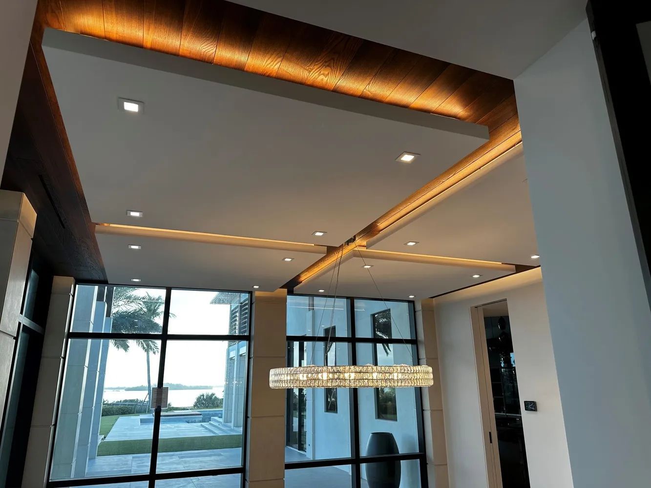 Modern interior with recessed lighting, glass walls, and a hanging chandelier overlooking a waterfront view
