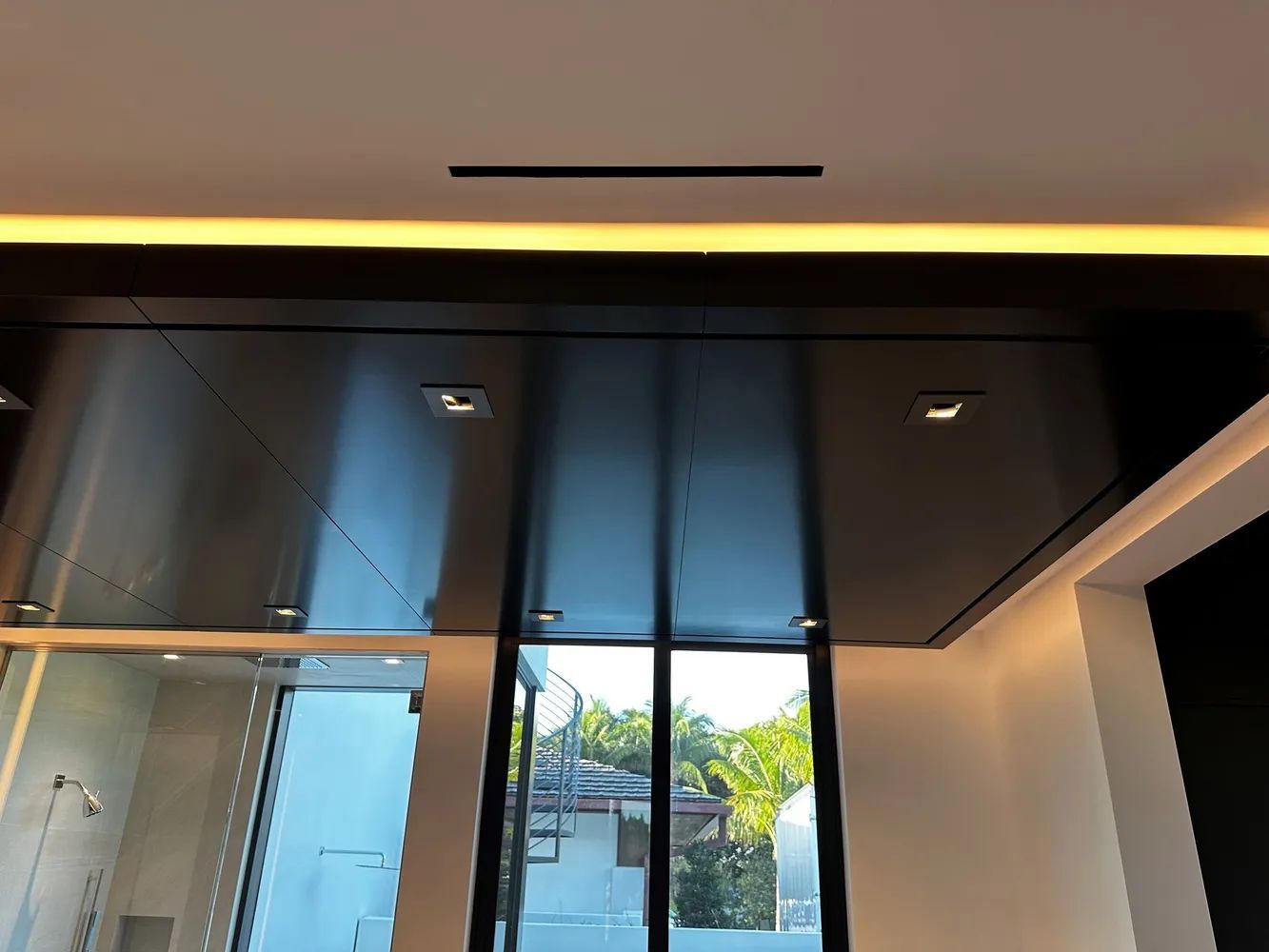 Modern glass entryway with dark ceiling panels and a view of trees outside