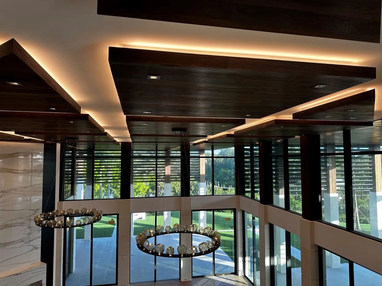 Modern interior with glass walls, wood ceiling beams, and a circular chandelier over a stairwell
