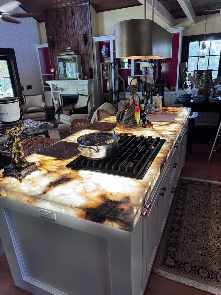 Kitchen island with a large marble-like countertop, stovetop, and stools in a modern open-plan room