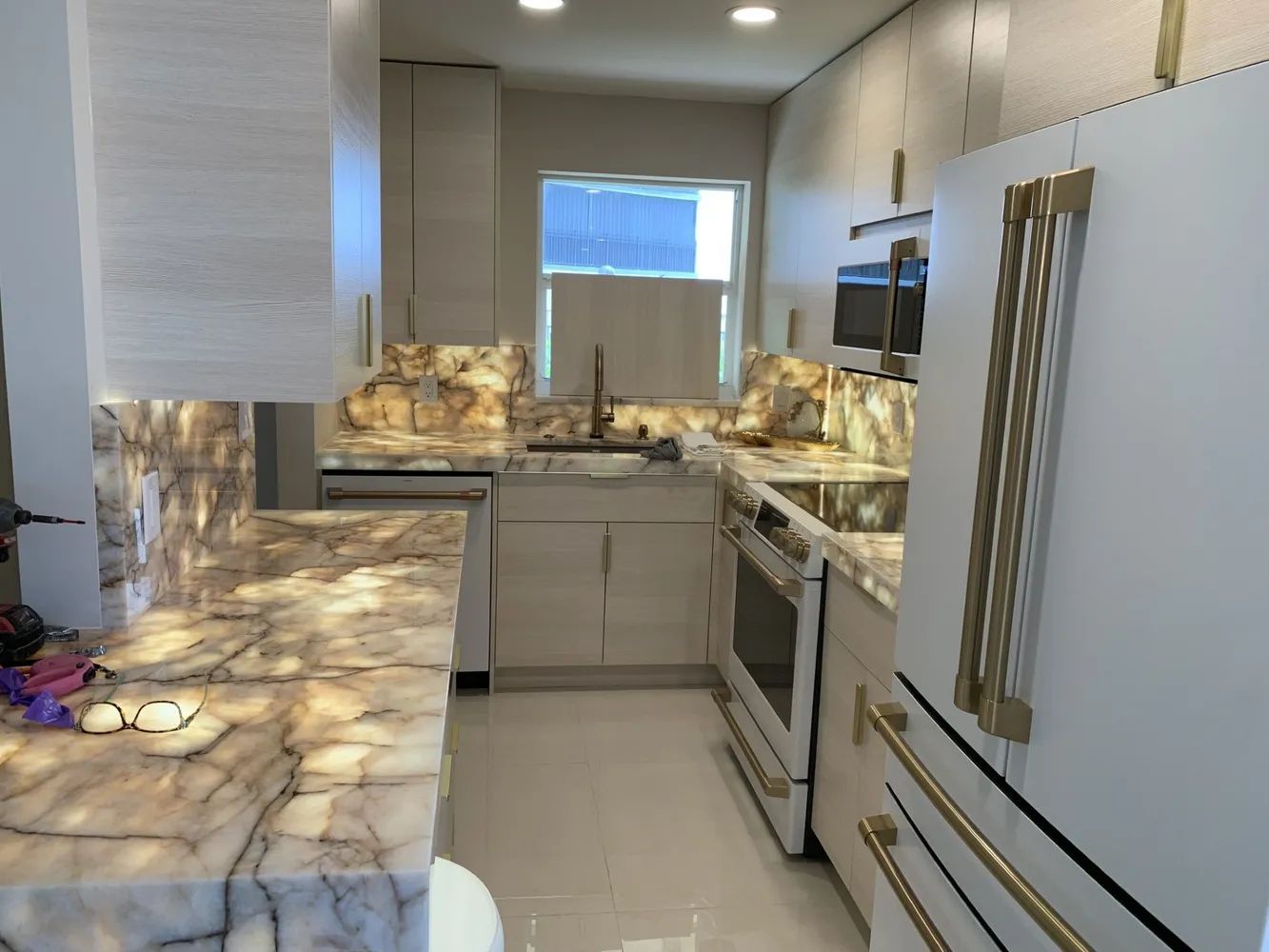 Modern kitchen with white cabinets, marble-pattern countertops, stainless appliances, and a window over the sink