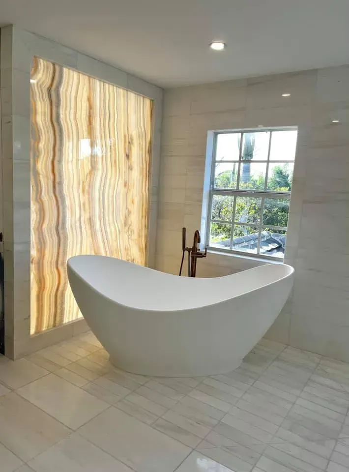 Modern bathroom with a freestanding white bathtub beside a window and backlit textured wall panel