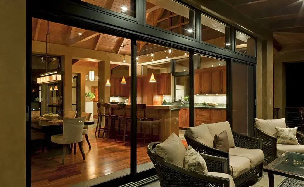 Modern open-air living room and kitchen with warm wood interior and cushioned patio seating at night