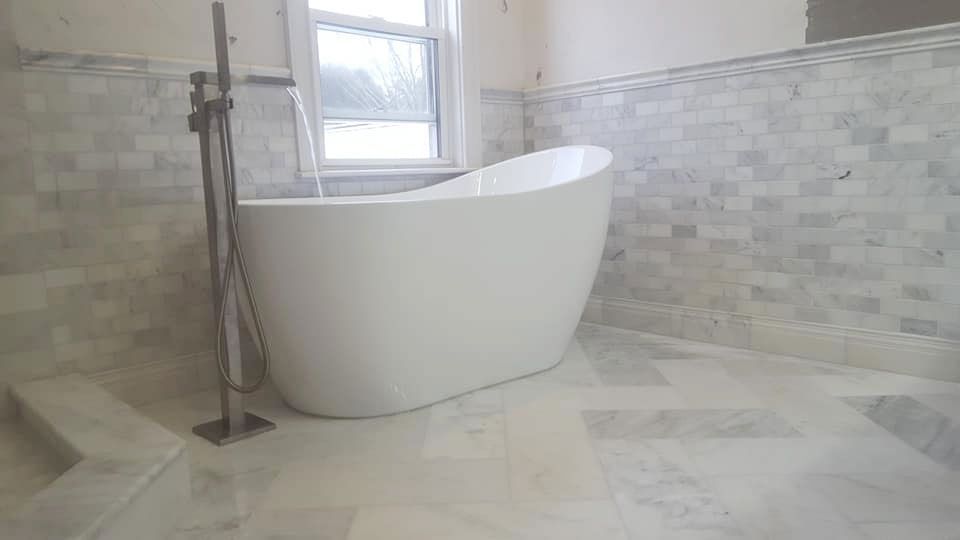 White freestanding bathtub in a bathroom with marble tile walls and floor.