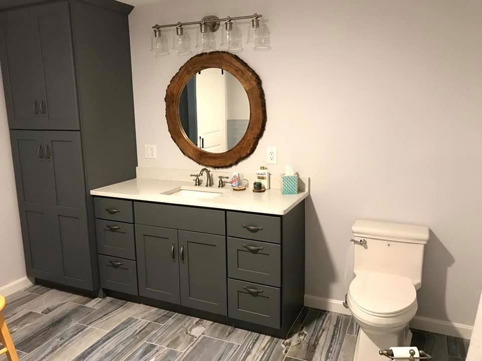 Bathroom with gray cabinets, a wood-framed mirror, white countertop, and patterned floor.