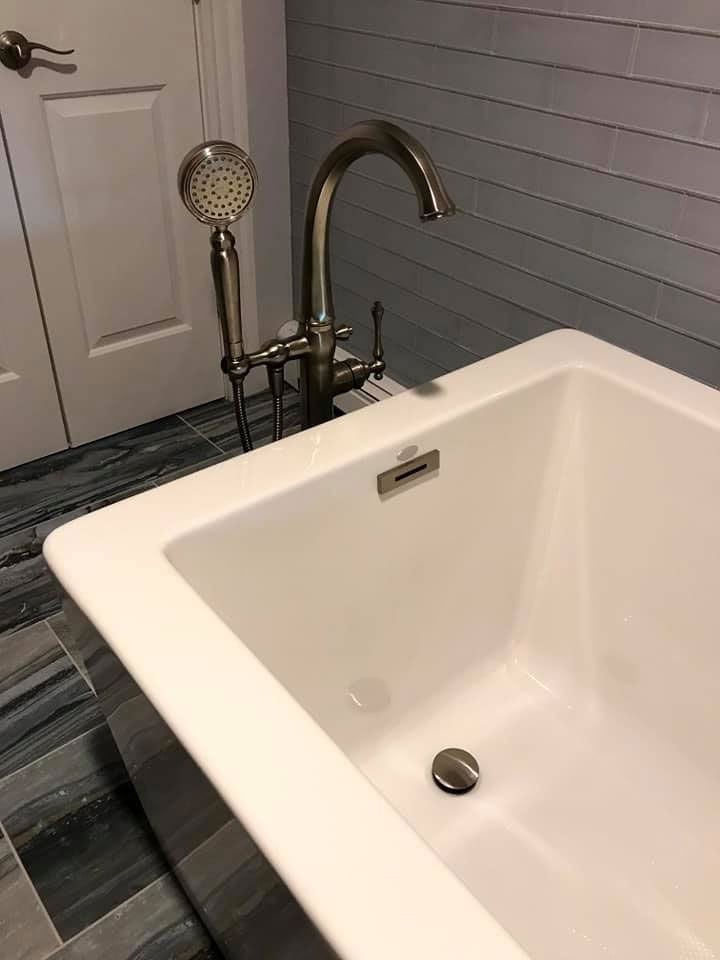 White bathtub with metallic faucet and handheld shower.  Gray tile backsplash and blue tile floor.
