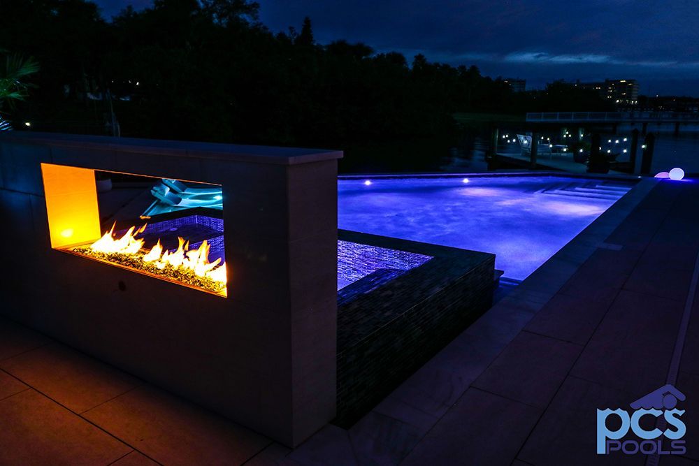 A fire pit next to a swimming pool at night.