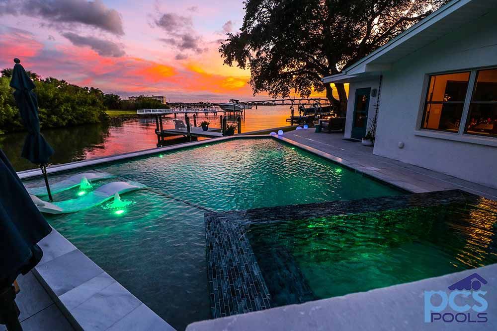 A large swimming pool in front of a house with a sunset in the background.