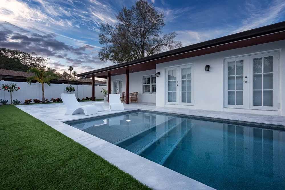 A white house with a large swimming pool in front of it.