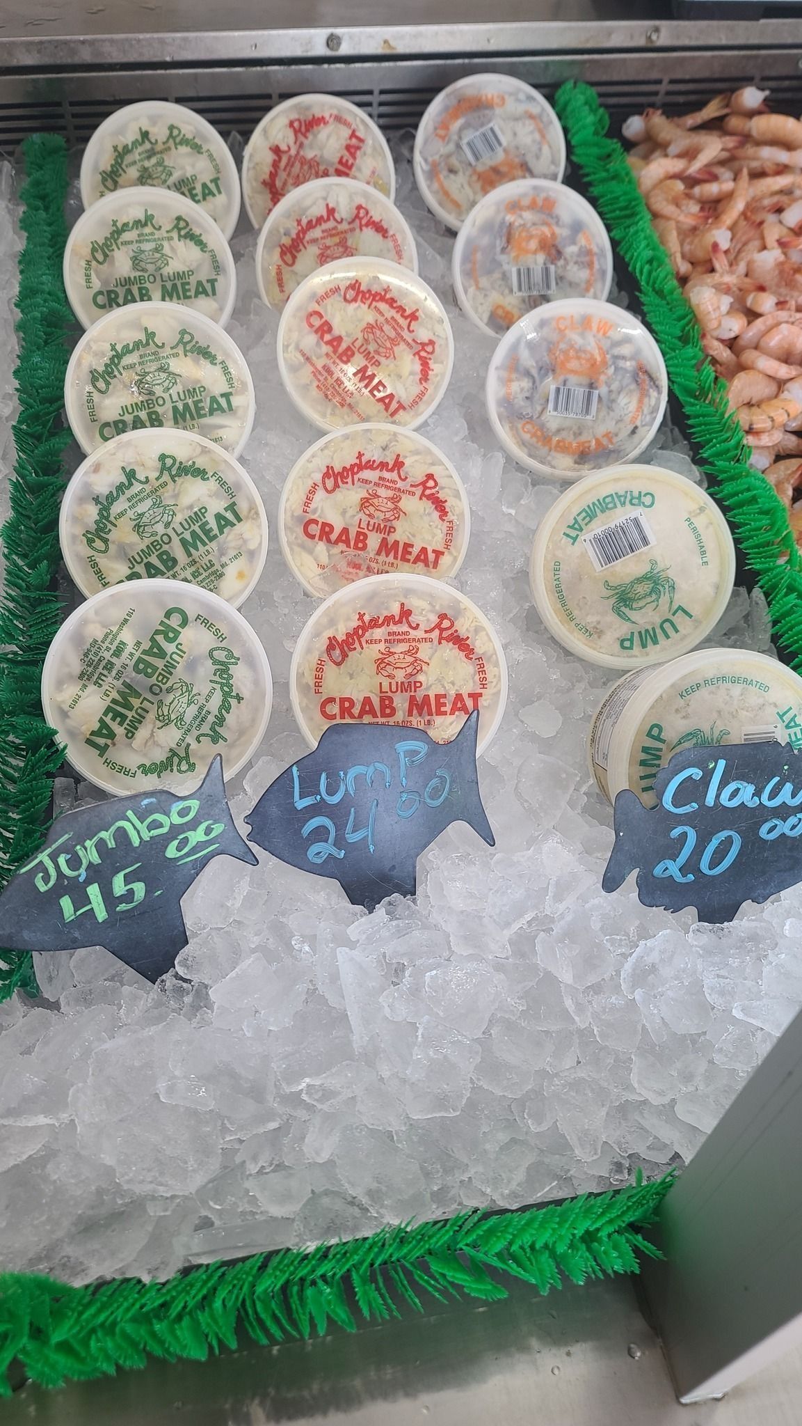 A seafood display case filled with ice, featuring containers of various crab cakes priced with chalkboard signs.