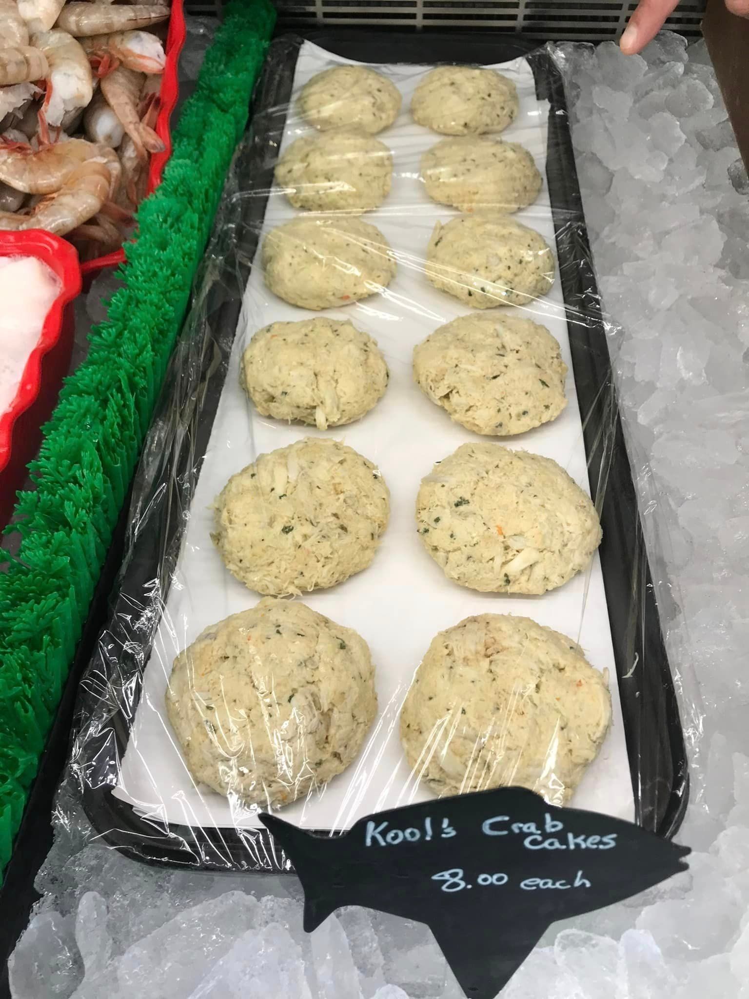 A tray of 12 round, seasoned crab cakes on ice at a market, labeled 