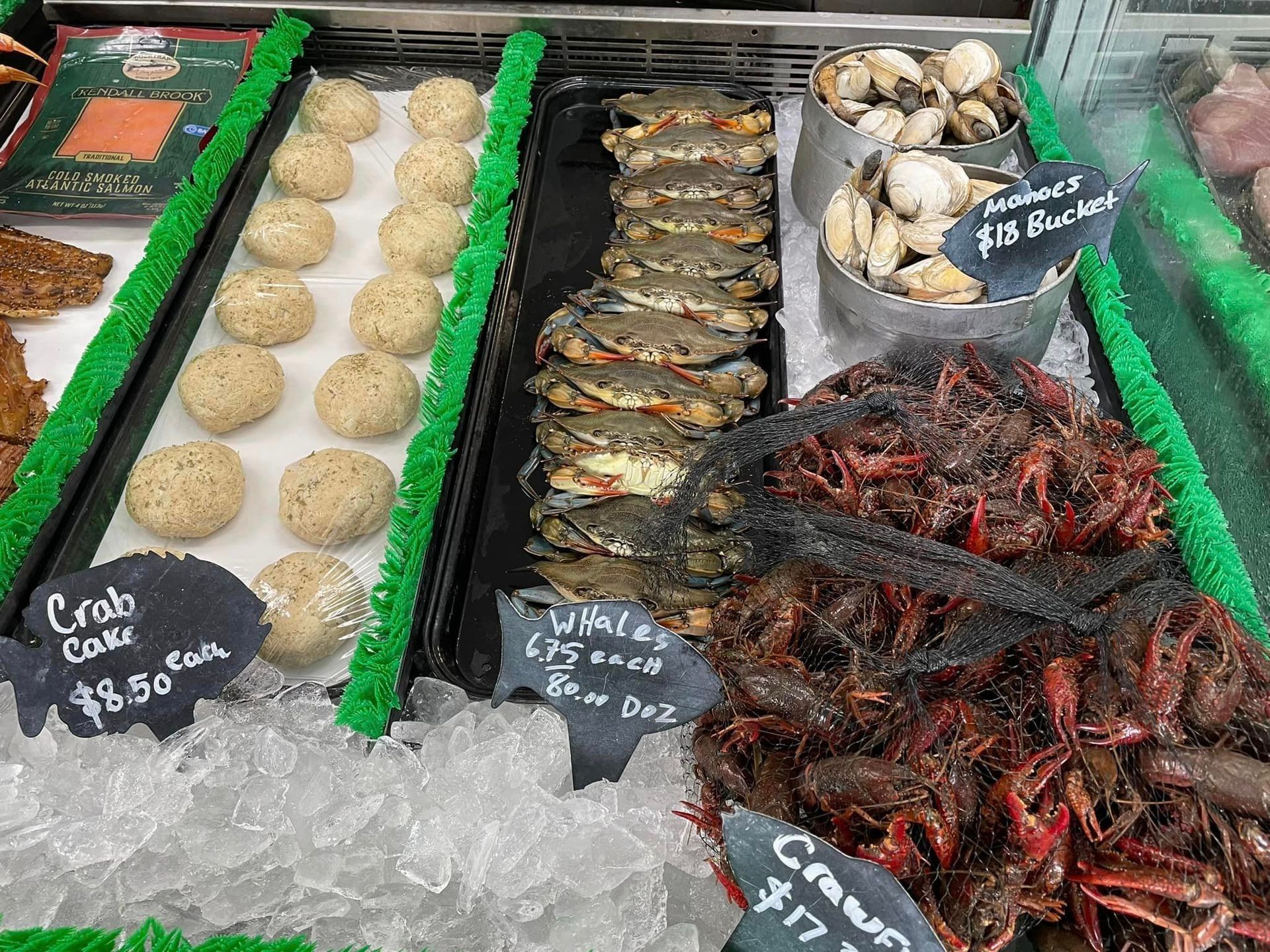 A seafood market display case featuring crab cakes, whole blue crabs, small buckets of shellfish, and crawfish on ice.