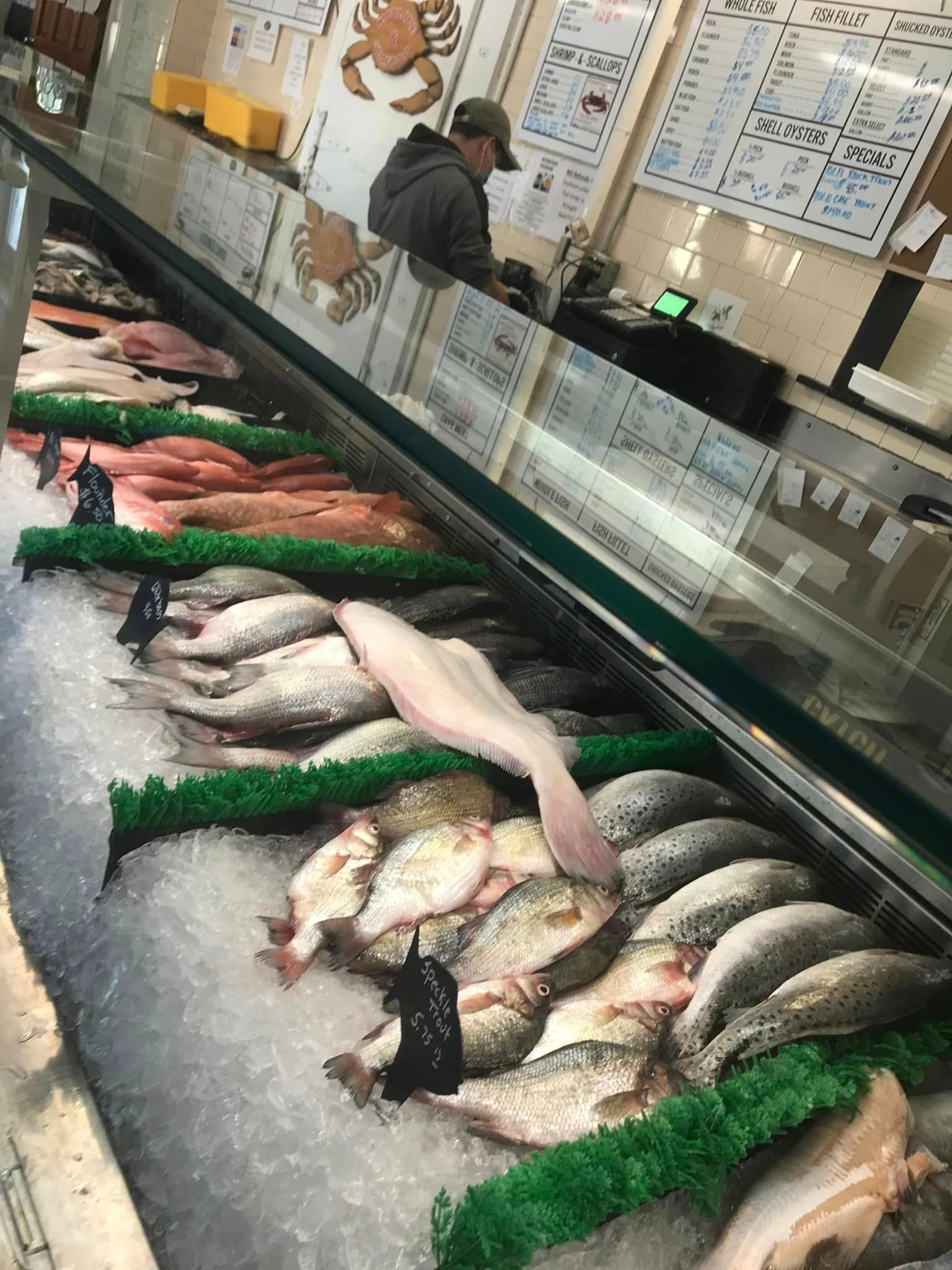 A variety of fresh fish laid out on beds of ice in a refrigerated display case at a market, with a worker in the back.