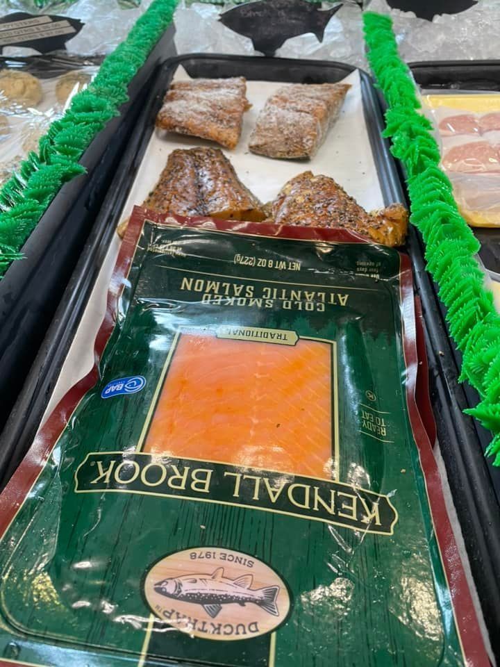 A package of Kendall Brook cold smoked Atlantic salmon sits next to other prepared fish fillets in a grocery display case.