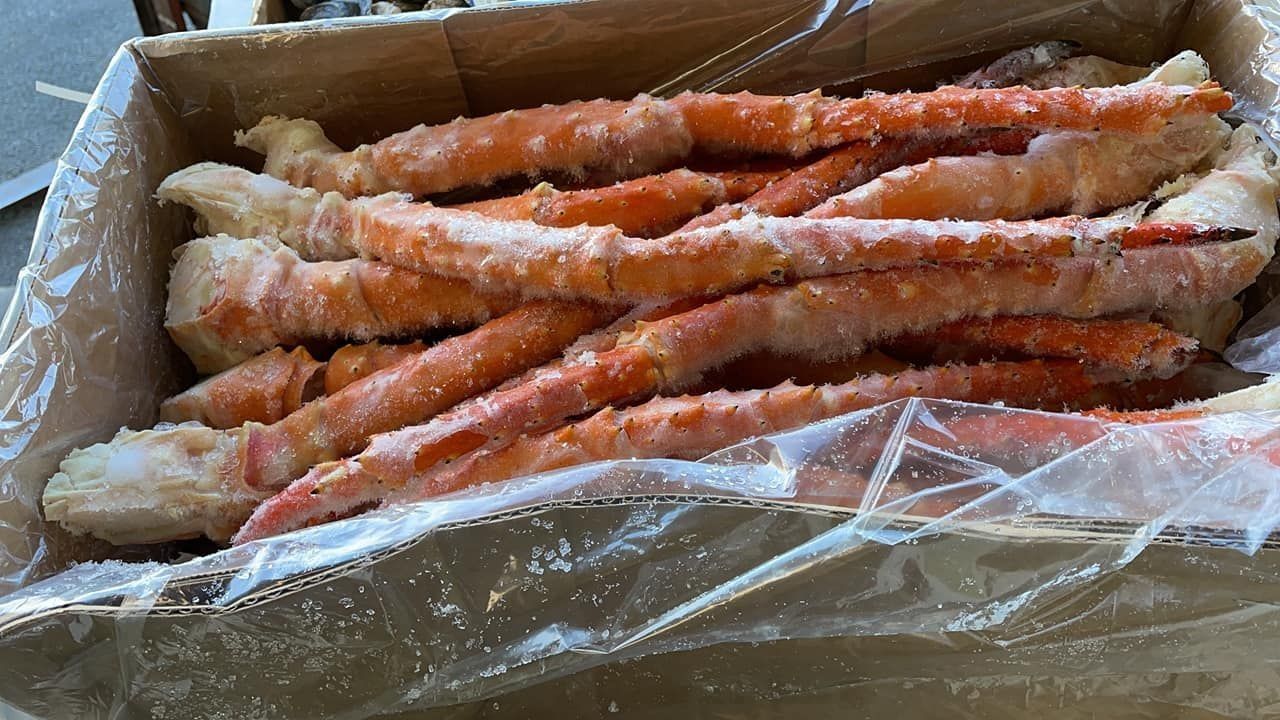A cardboard box filled with frozen, orange and white king crab legs covered in a thin layer of ice.