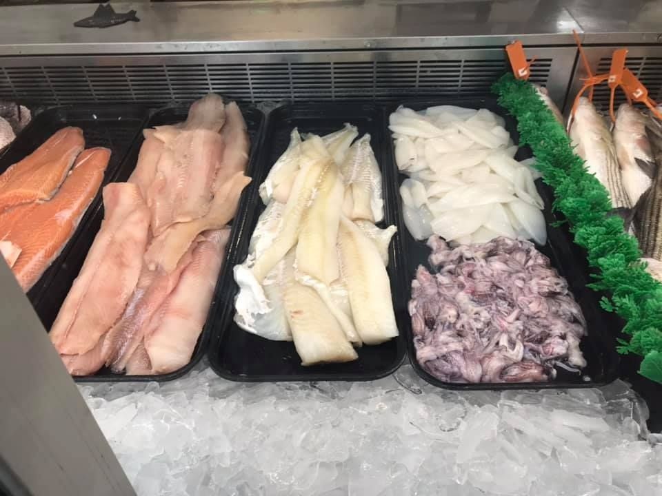 A seafood display case filled with trays of various raw fish fillets and shellfish resting on a bed of ice.