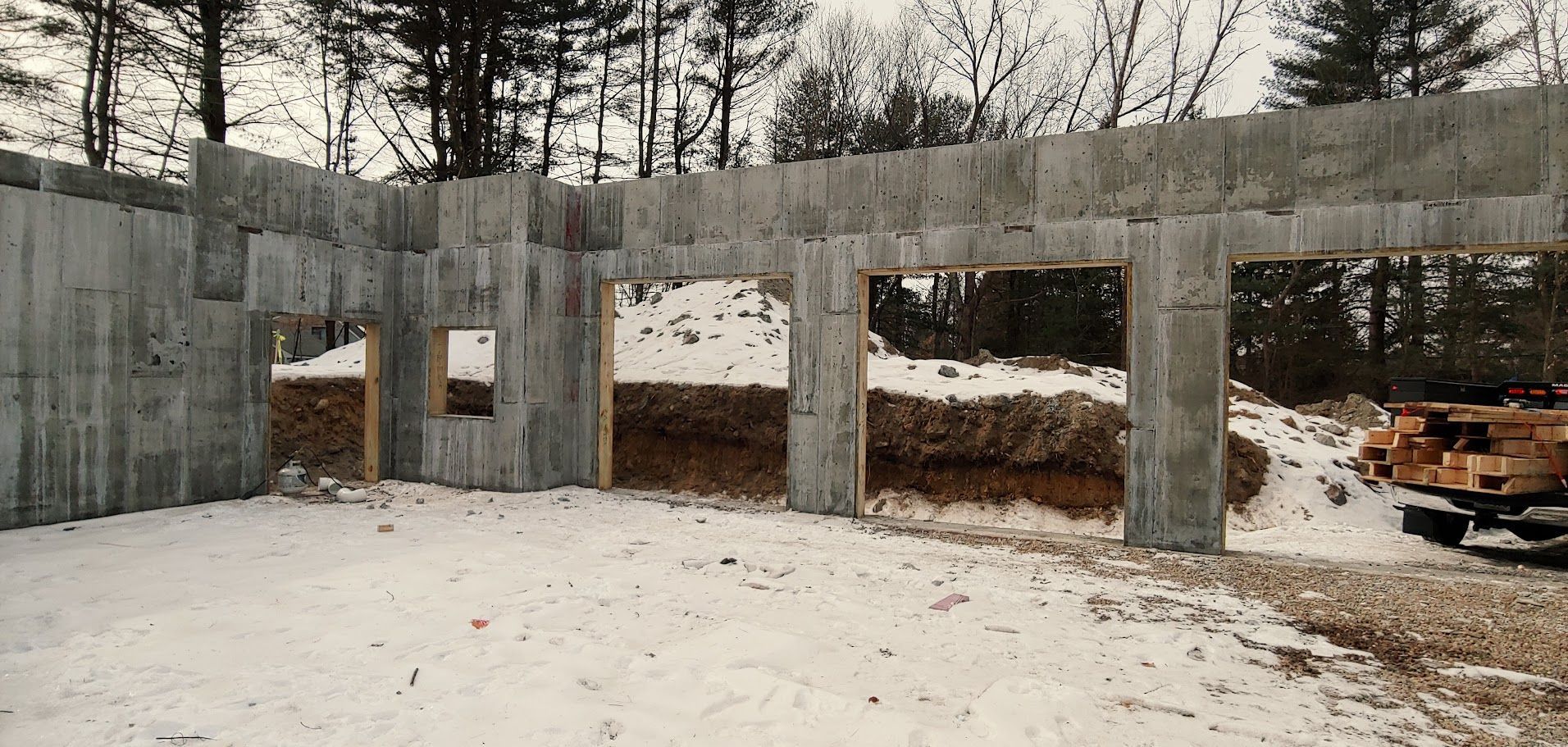 A concrete wall is being built in the snow with trees in the background.