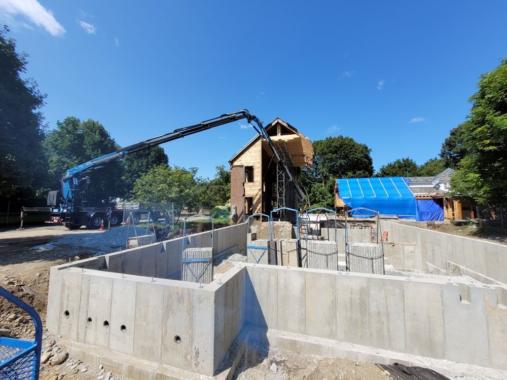A crane is pouring concrete into a foundation of a house under construction.