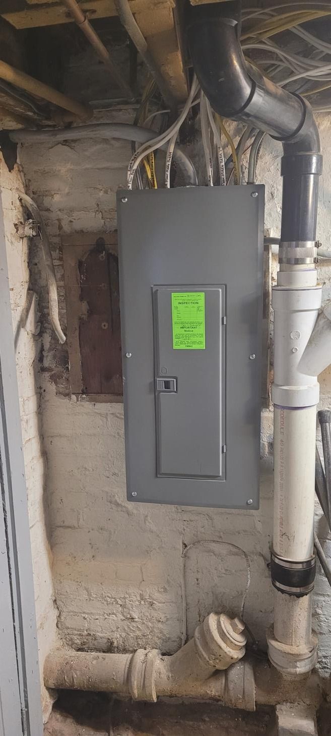 Electrical panel on a concrete wall, with pipes nearby in a basement setting.