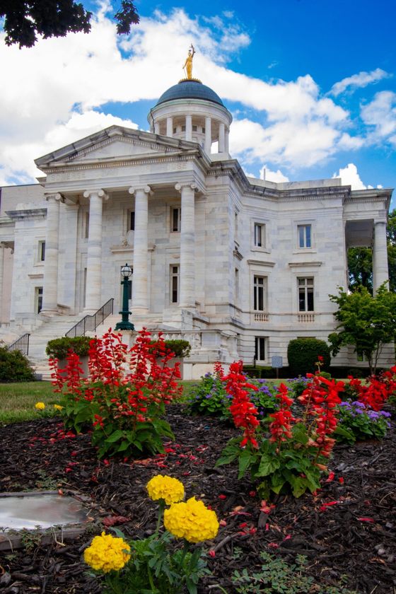White marble domed building with gold top, framed by red and yellow flowers under a blue sky