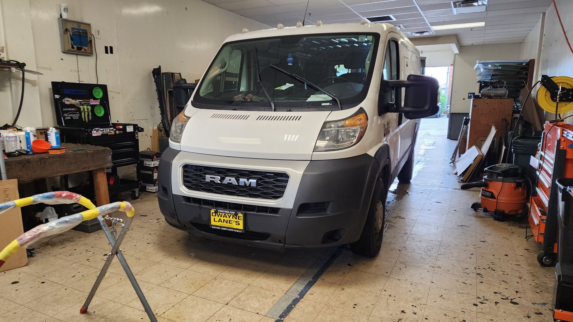 White RAM van inside a garage, likely for repair. Tools and equipment surround it.
