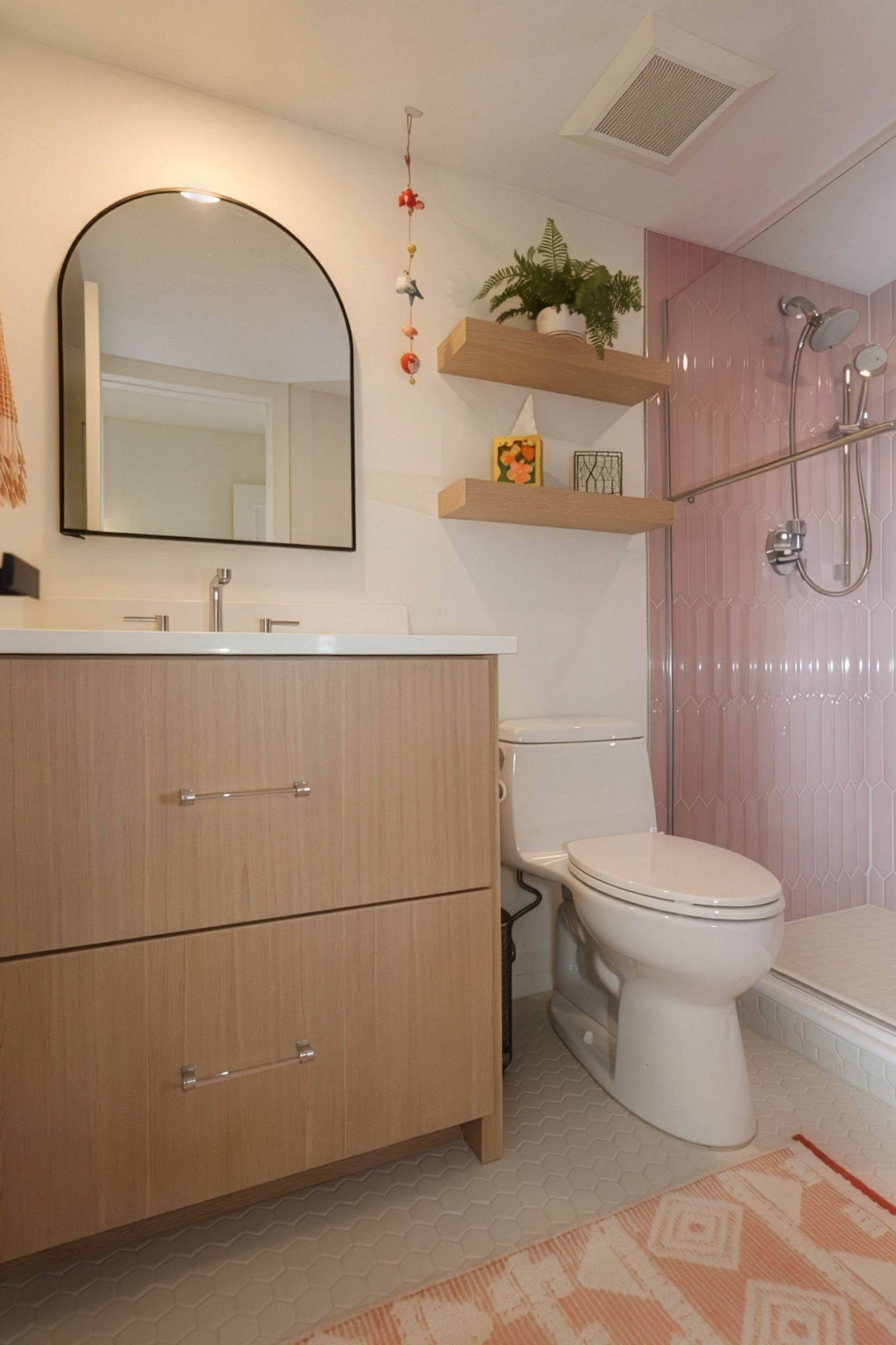 Small pink and white bathroom with vanity, mirror, toilet, shower curtain, and wall shelves with plants