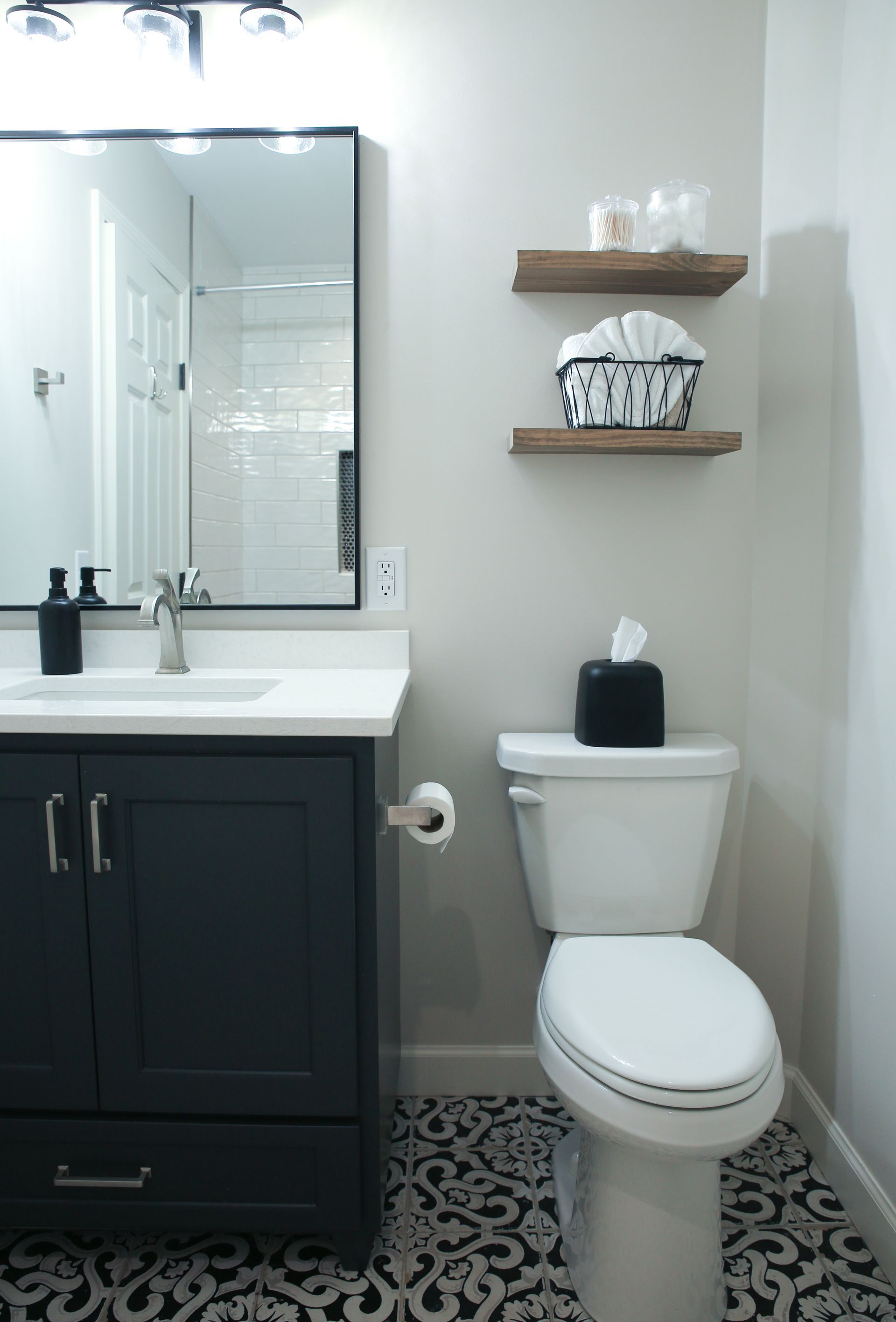 Small bathroom with white sink, dark vanity, toilet, mirror, and patterned black-and-white floor.