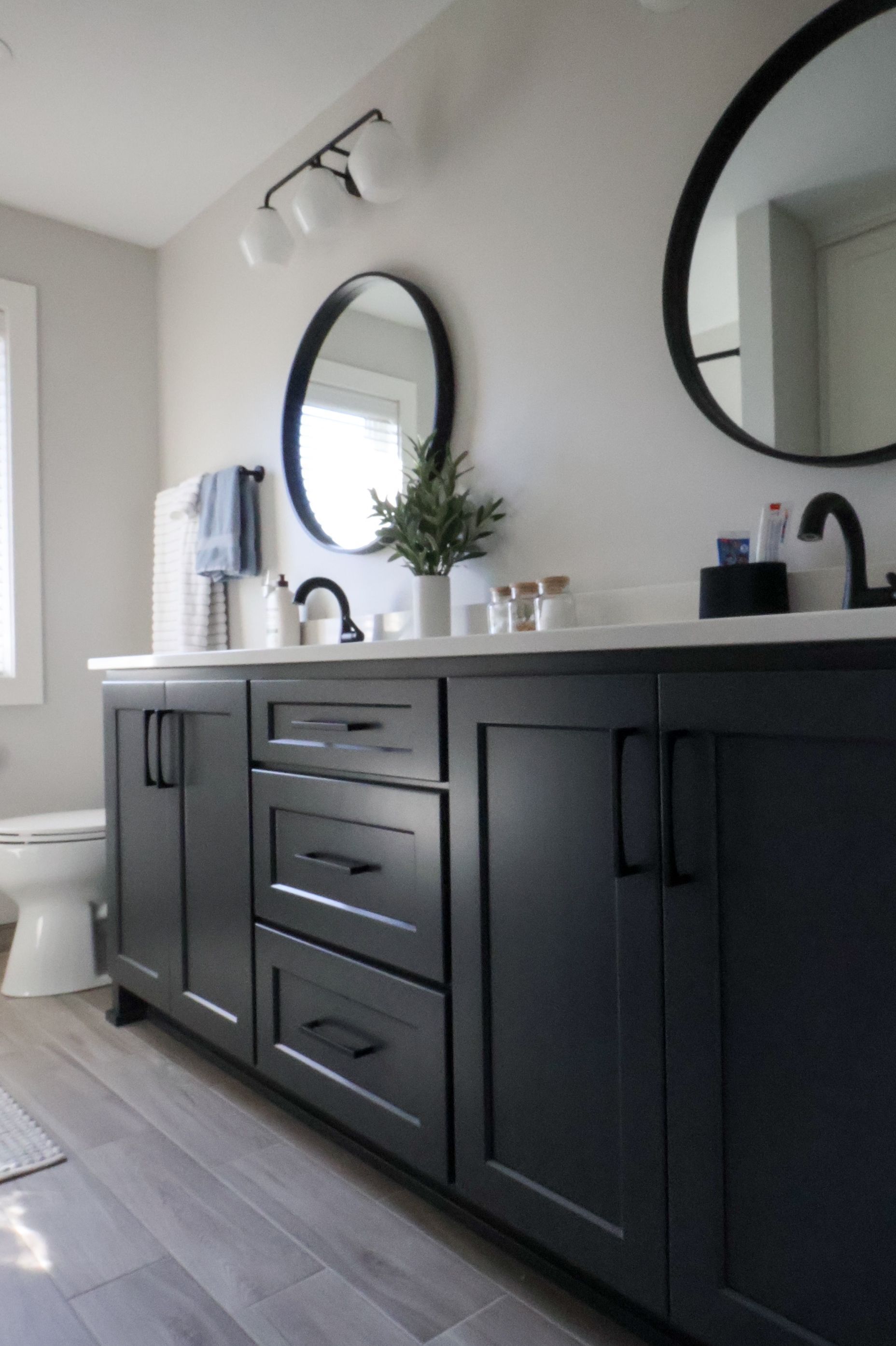 Modern bathroom with dark vanity, round mirrors, white countertop, and black fixtures.