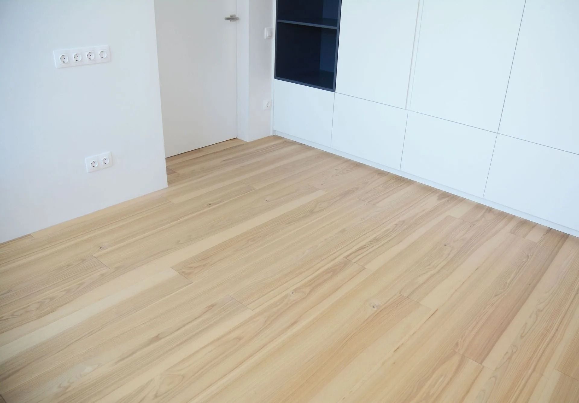 Light wood floor in a white room with white cabinets and a black screen.