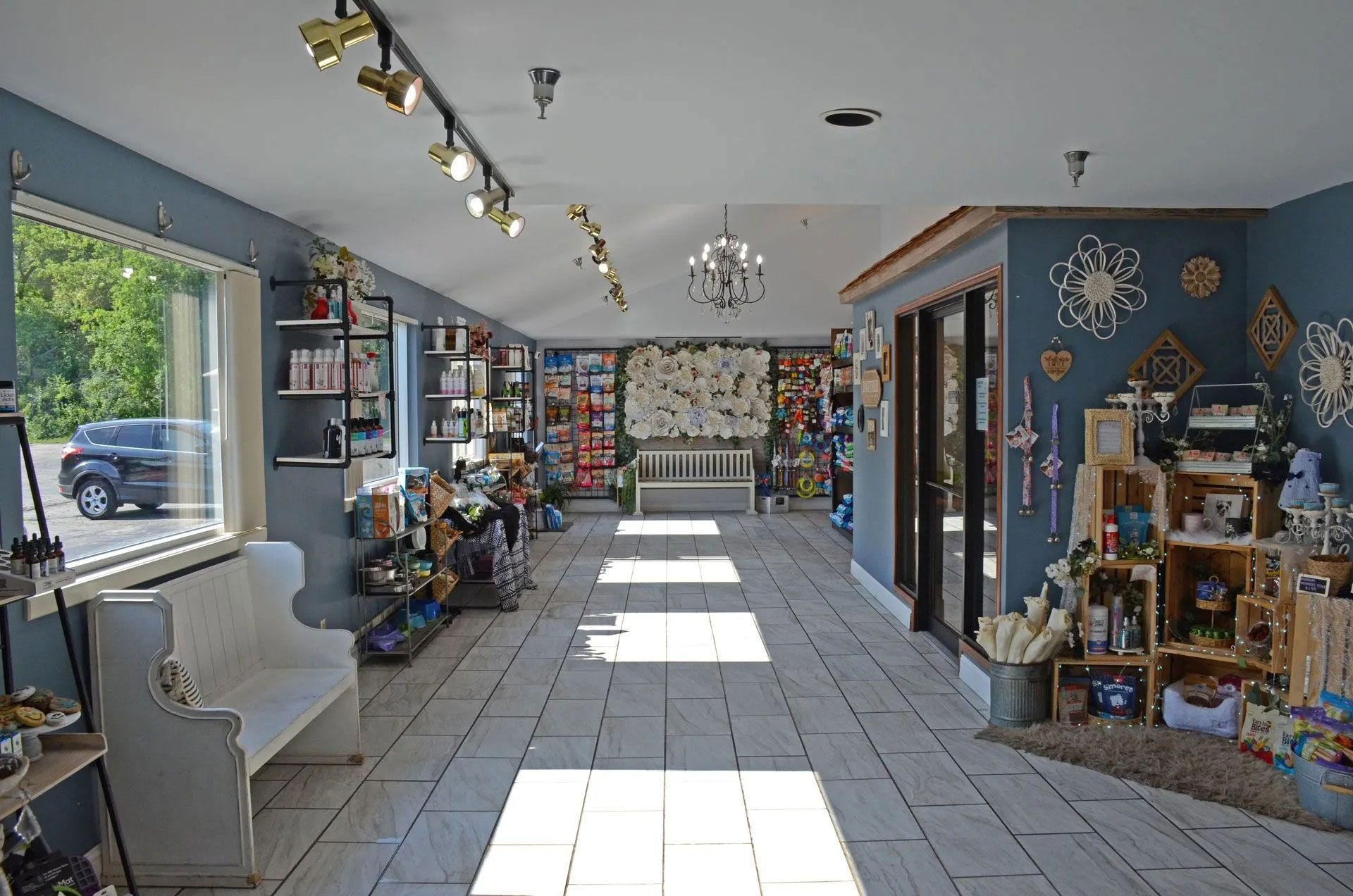 A sunlit interior view of a boutique shop with light-colored tile floors, blue-gray walls, shelves of goods, and seating.