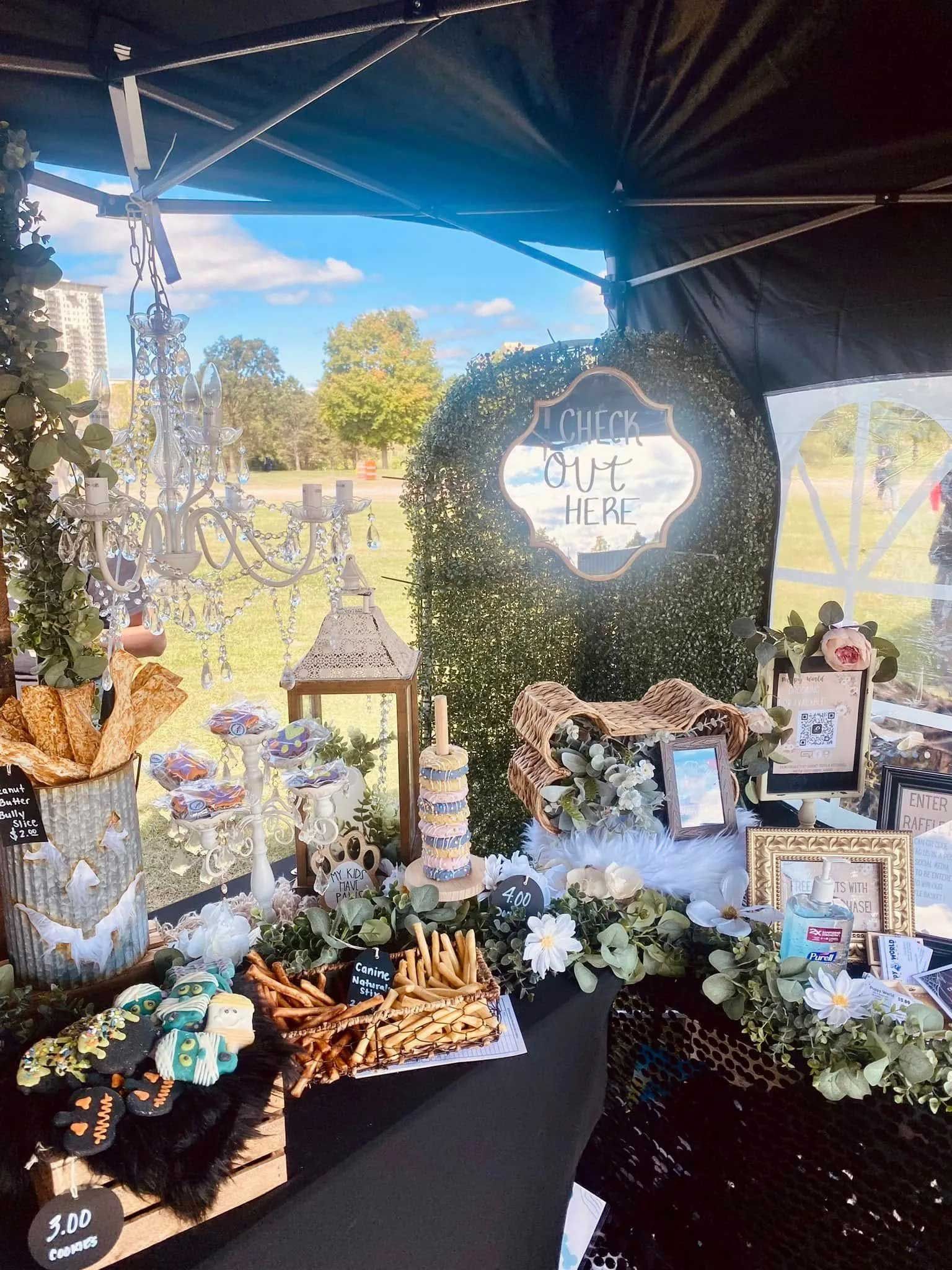 A decorated event table under a black tent featuring greenery, a chandelier, a 
