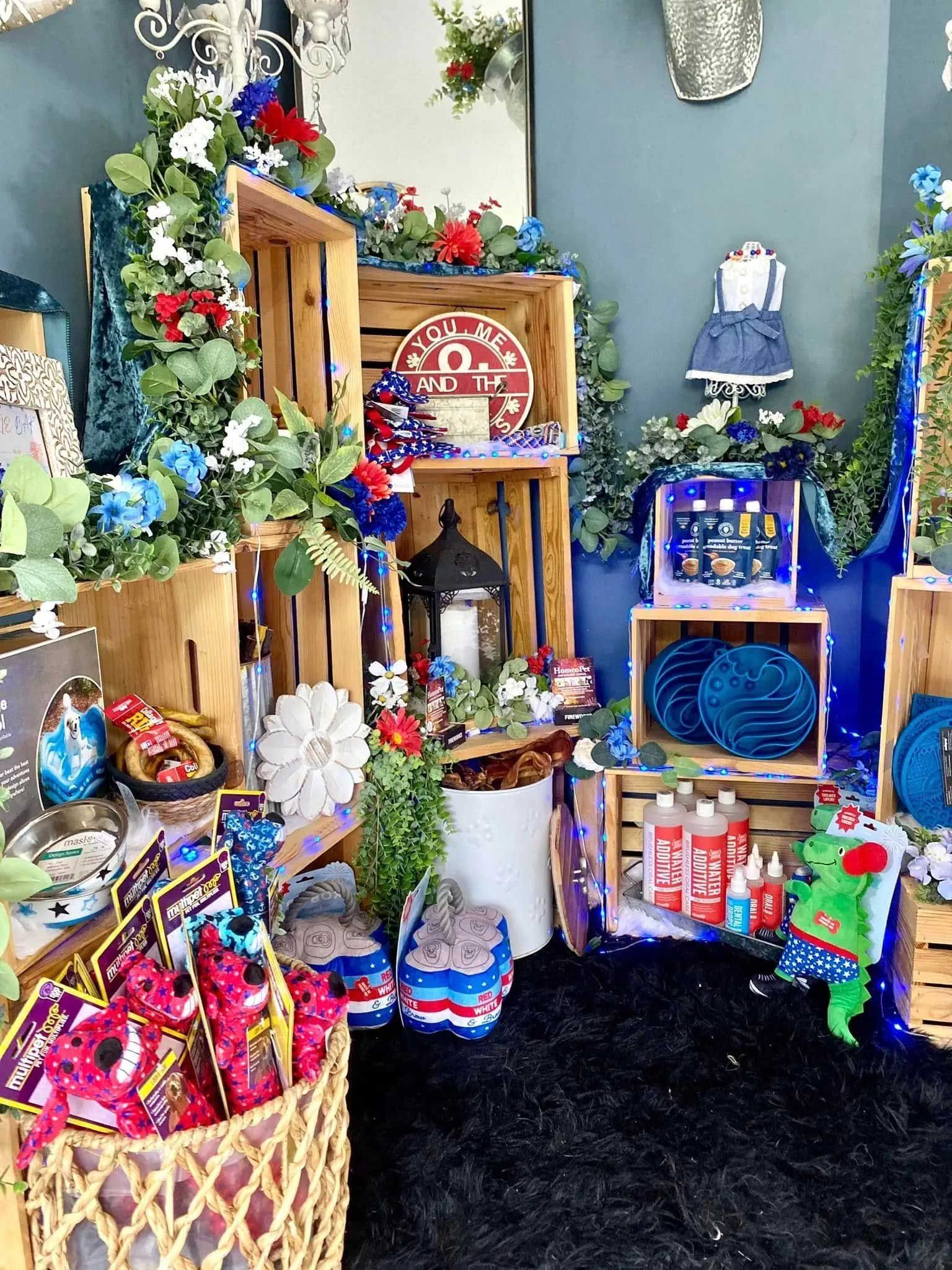 A festive display with wooden crates, floral decorations, blue items, and snacks on a black rug against a blue wall.