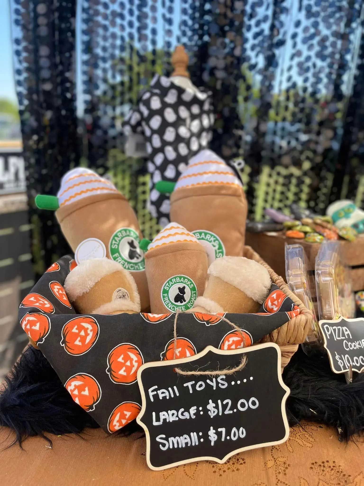 A basket filled with plush coffee-themed dog toys, priced at $7 for small and $12 for large, set against a dark background.