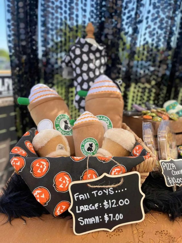 A basket filled with plush coffee-themed dog toys, priced at $7 for small and $12 for large, set against a dark background.