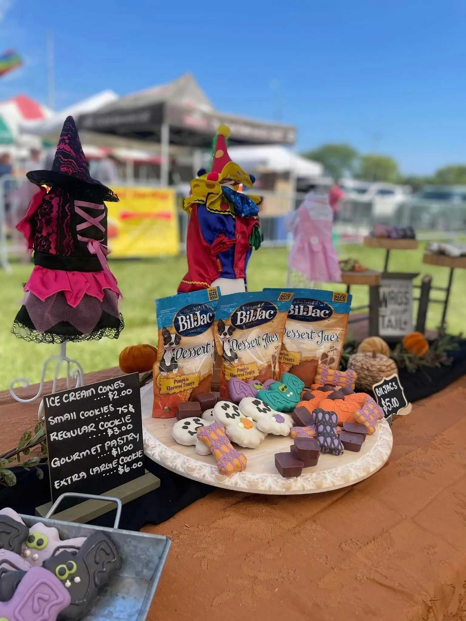 A table display at an outdoor event featuring a witch hat, snacks, and themed treats on a decorative tray.