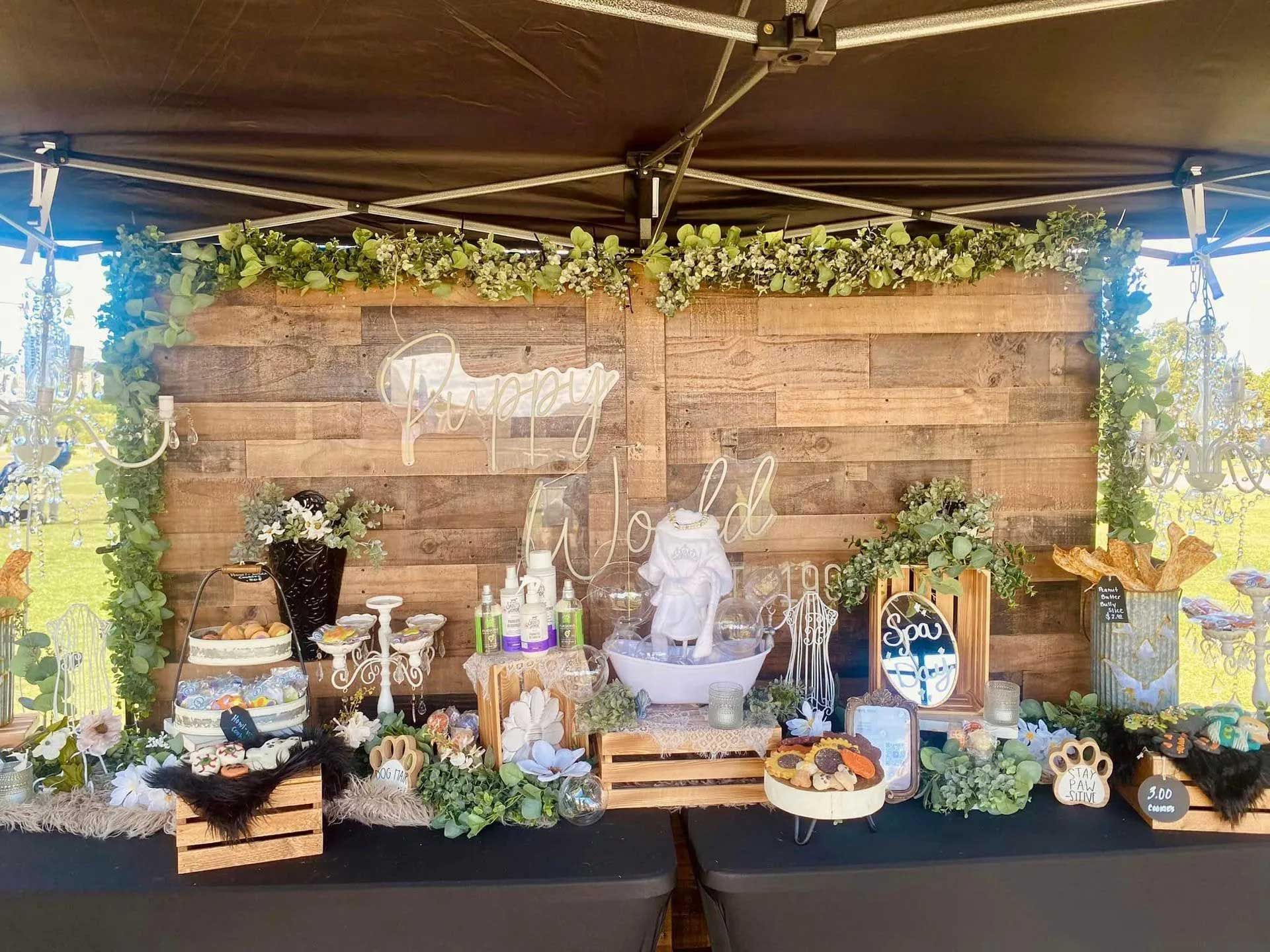 A wooden backdrop display with greenery, fairy lights, and tiered crates holding various food and decorative items.