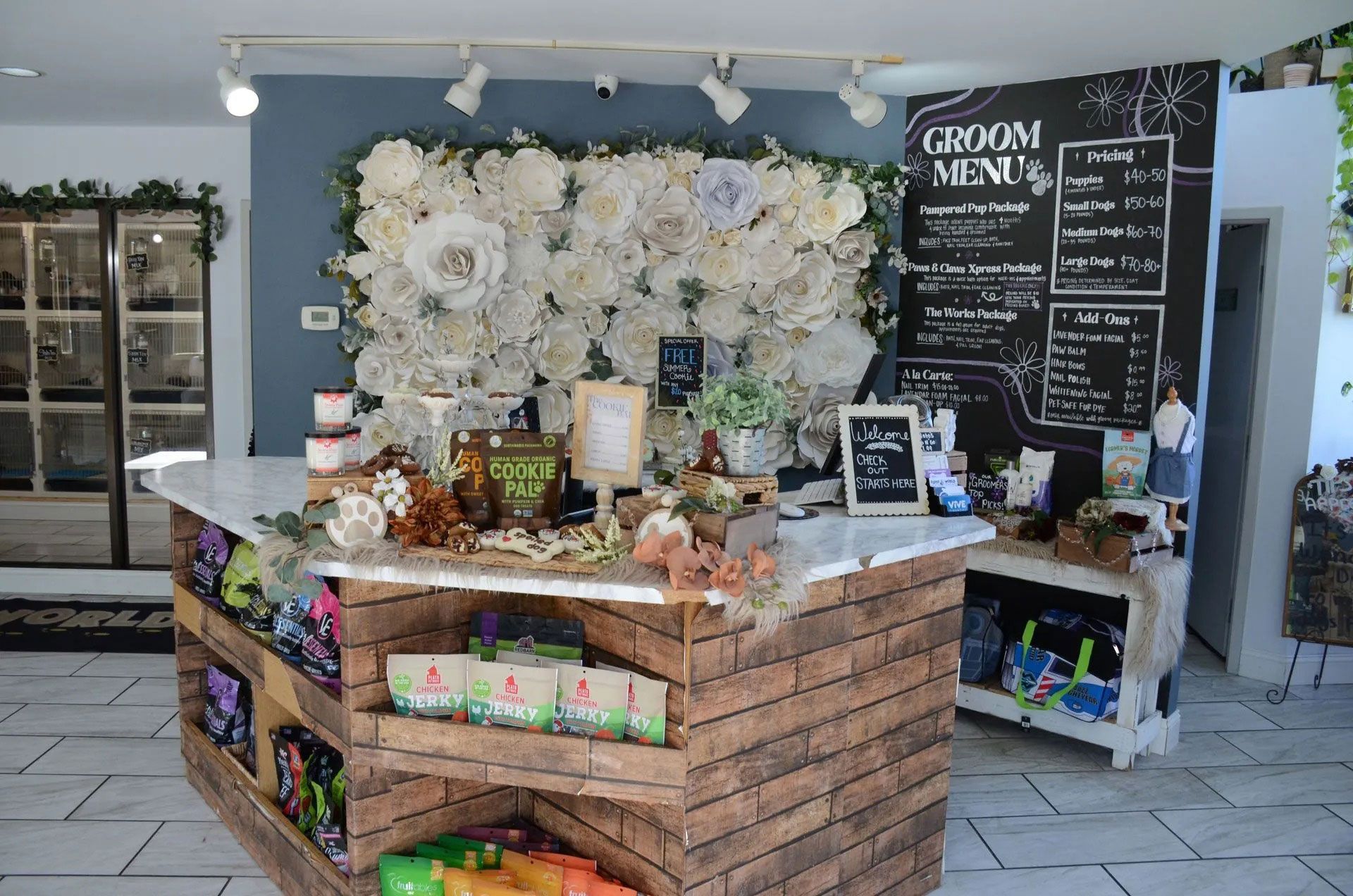 A rustic brick reception desk in a pet grooming salon, featuring a decorative flower wall and a chalkboard menu.