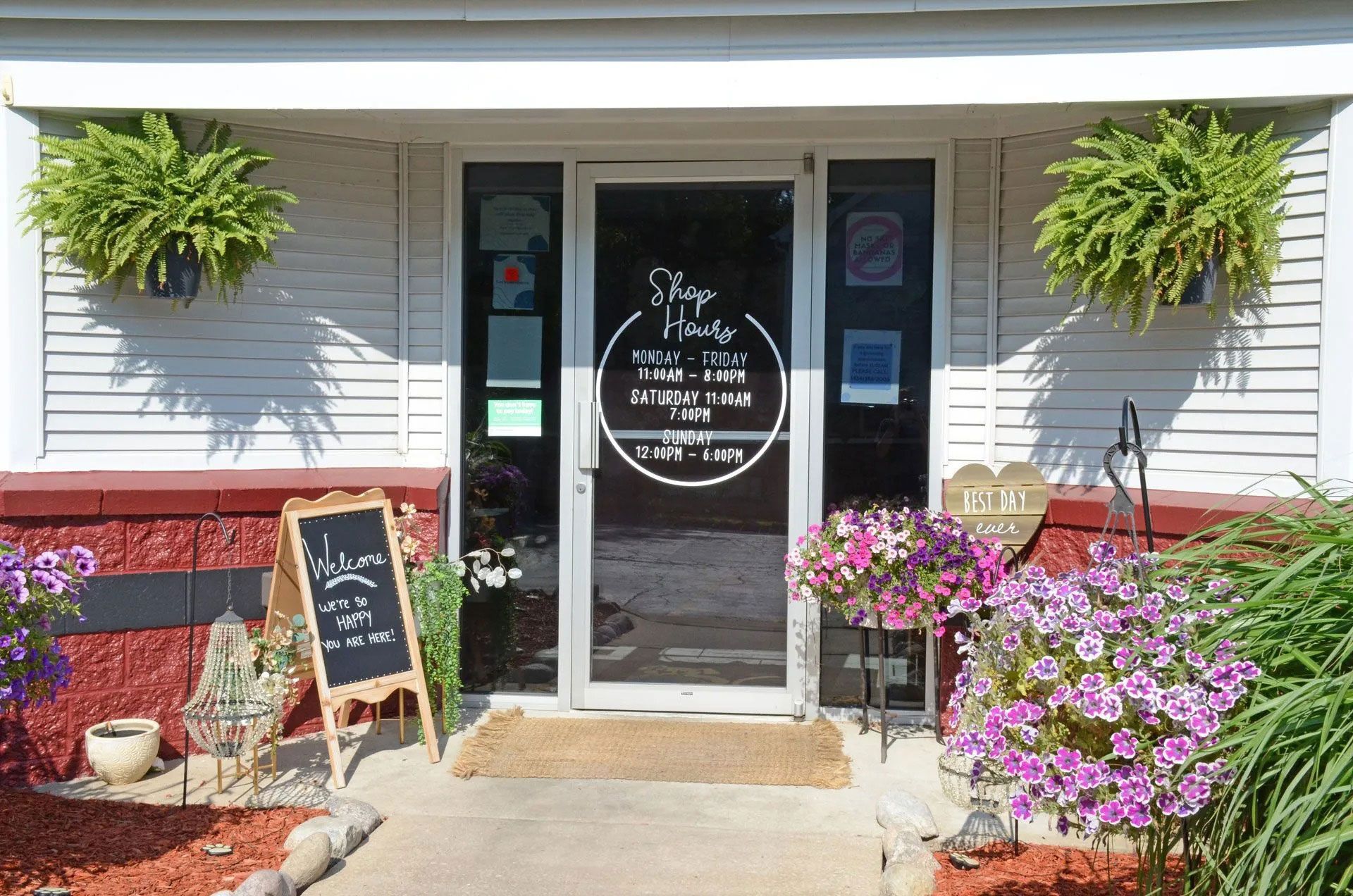 The storefront of a business with a glass door, hanging flower baskets, and a sidewalk chalkboard sign.