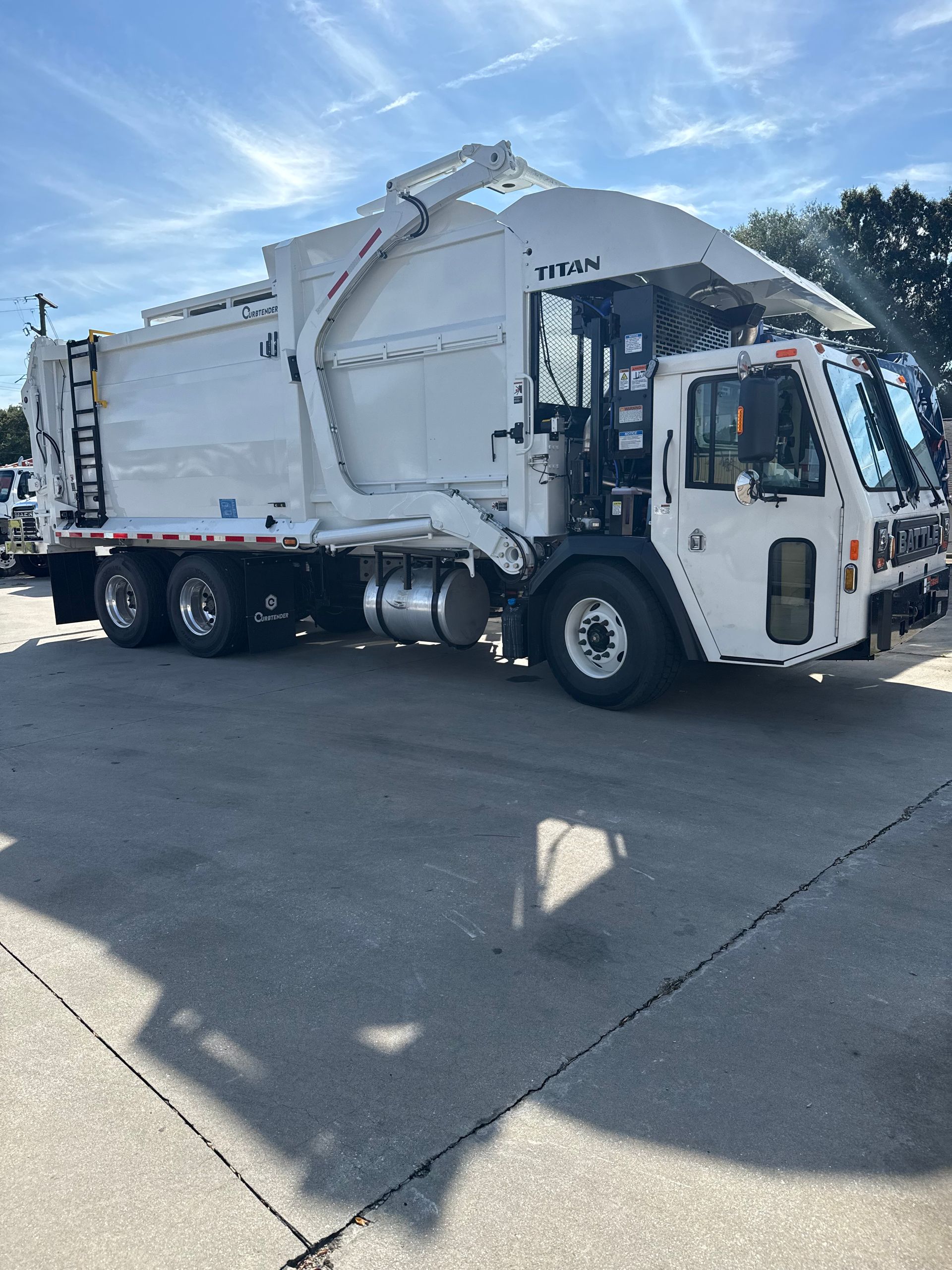 A white truck is parked in a gravel lot next to a forklift.