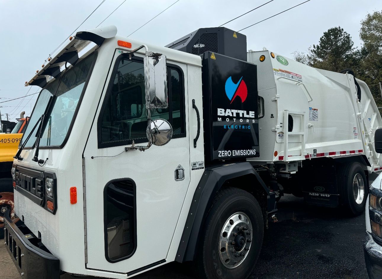 A white garbage truck is parked on the side of the road.